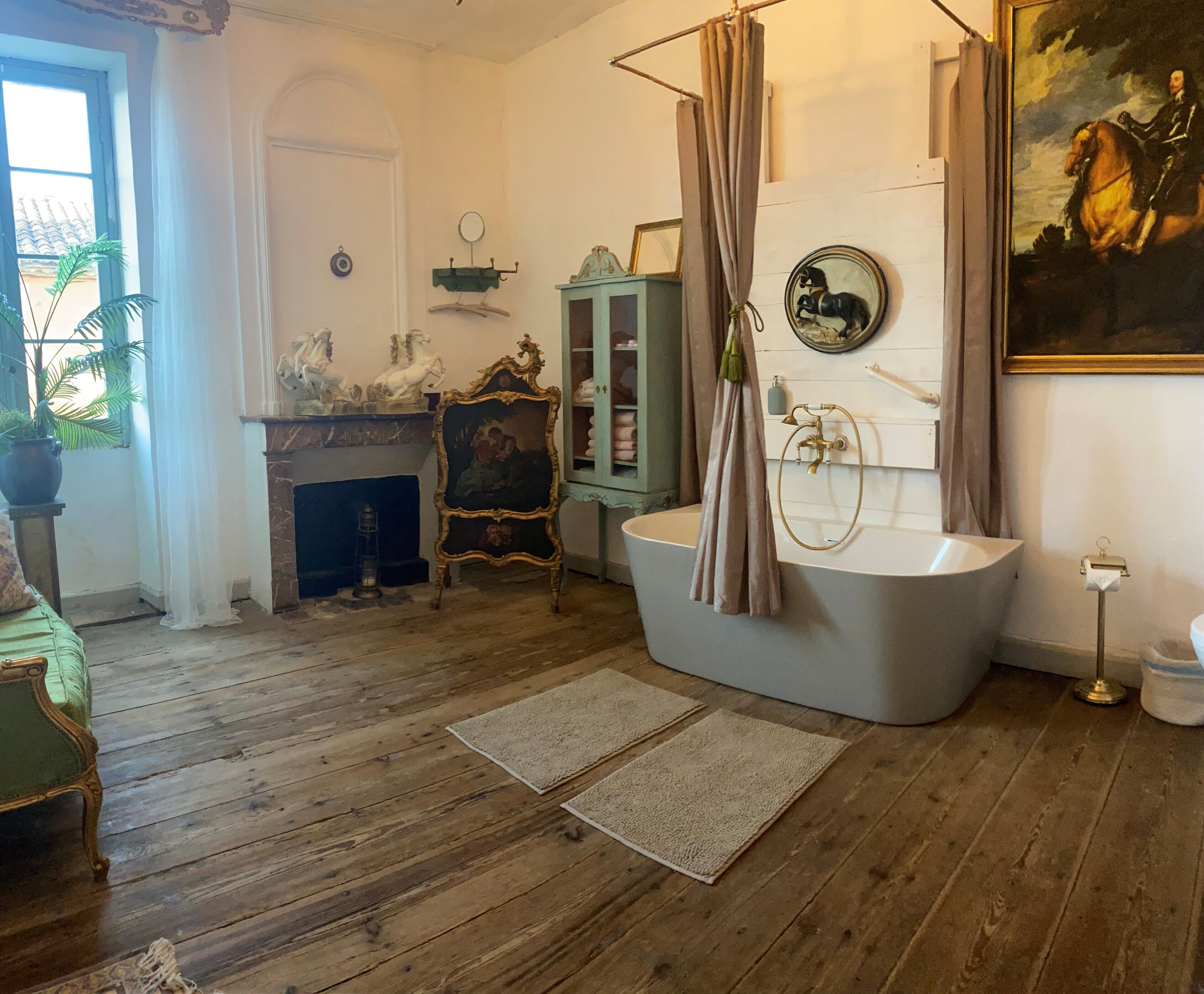 Een kamer met een badkuip, een open haard, een schilderij en een spiegel aan de muur.