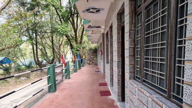 A corridor with tiled walls and a red floor, leading to a building with large windows and a tiled exterior.