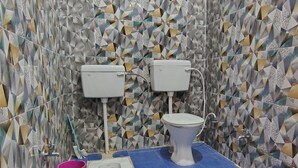 A bathroom with two toilets, a bidet, a blue tiled floor, and a patterned tile wall.