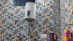 A bathroom with a geometric patterned tile wall, a water heater, and a towel rack with colorful towels.