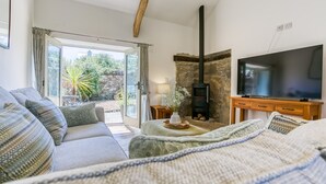 A cozy living room with a sofa, a television, a stone fireplace, and a view of the outdoors.