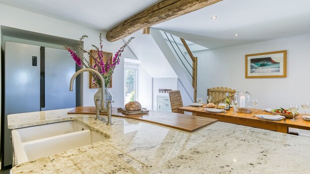 A modern kitchen with a marble countertop, a built-in sink, and a wooden ceiling beam.