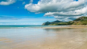 A beach with a clear sky, calm sea, and distant mountains.