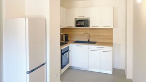 Une cuisine de taille réduite avec des meubles blancs, un four à micro-ondes, un évier et une cuisinière.
