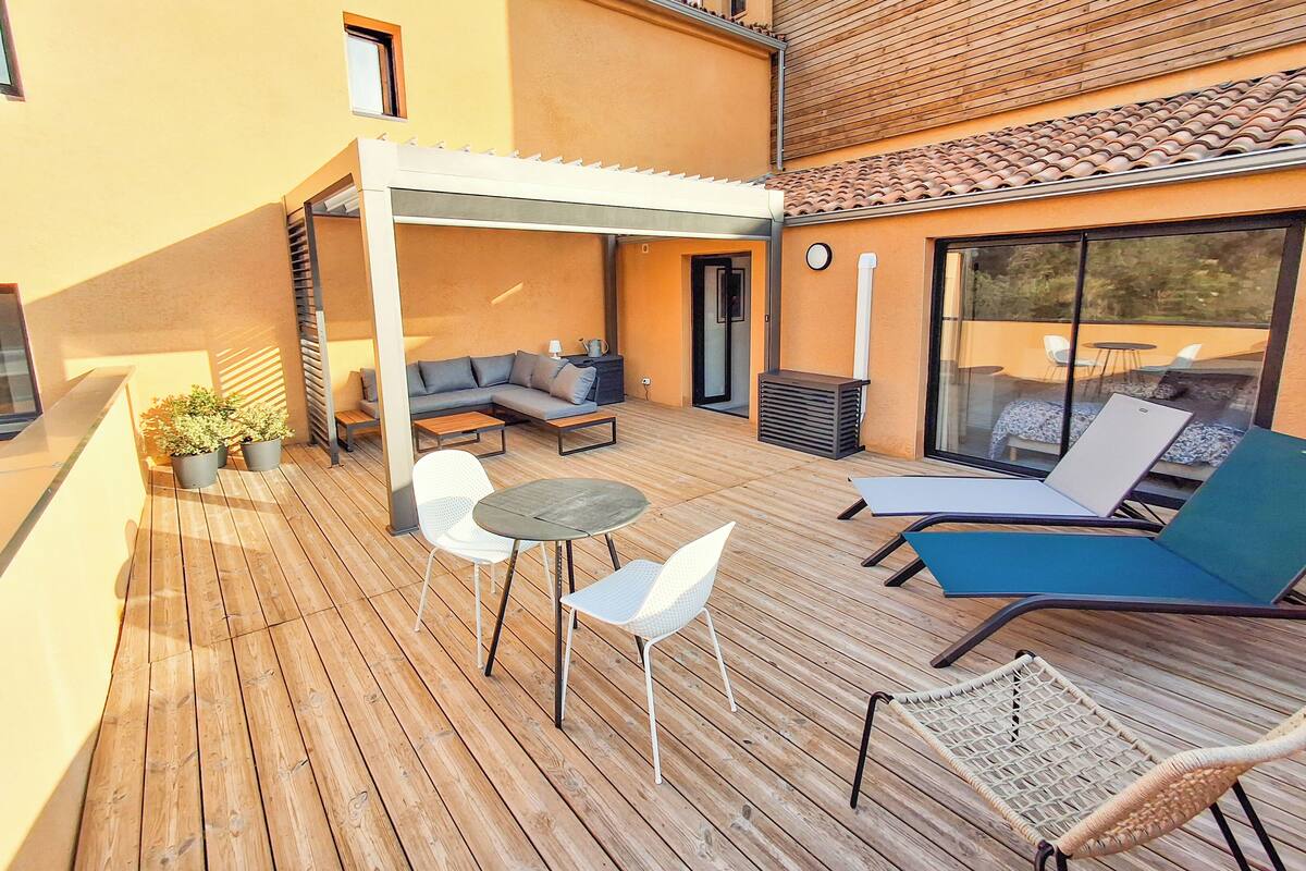 Una terraza de madera con mobiliario exterior, incluyendo un sofá, sillas y una mesa.