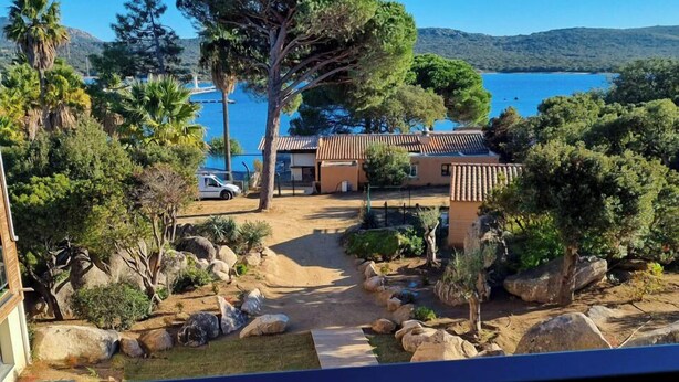 Une propriété située sur la côte, avec un chemin pavé menant à un bâtiment, le tout entouré de gros rochers et d’arbres.