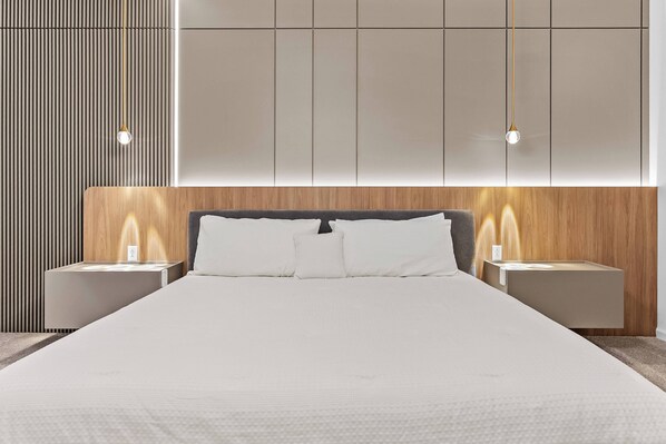 A modern bedroom with a large bed, wooden headboard, and bedside tables with integrated lighting.