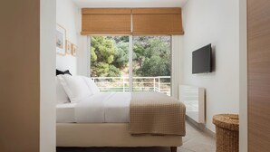 A bedroom with a bed, a television, a window with a view of trees, and a wicker basket. - Vouliagmeni Exclusive Residence (Vouliagmeni)