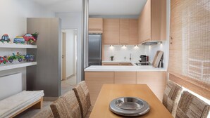 A modern kitchen with wooden cabinets, a stainless steel refrigerator, and a dining area with a wooden table and woven chairs. - Vouliagmeni Exclusive Residence (Vouliagmeni)