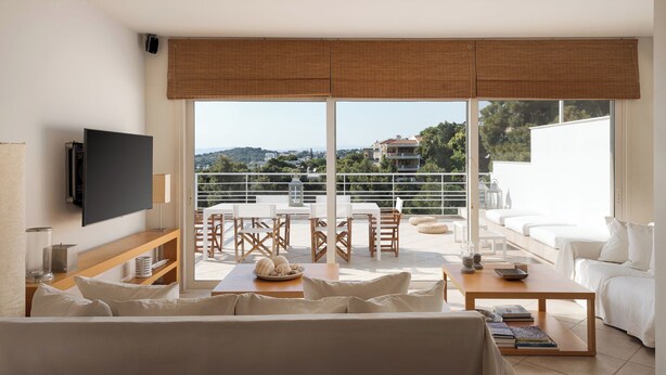 A modern living room with a large TV, a dining area with a table and chairs, and a balcony with a view of the city. - Vouliagmeni Exclusive Residence (Vouliagmeni)