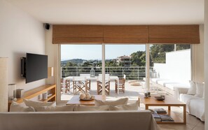 Uma sala de estar moderna com uma televisão grande, um espaço de jantar com mesa e cadeiras, e uma varanda com vista para a cidade.
