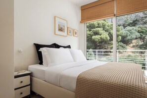 A bedroom with a bed, a nightstand, and a window with a view of trees.