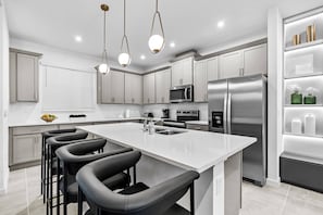 Una cocina moderna con una isla grande, electrodomésticos de acero inoxidable y taburetes negros.
