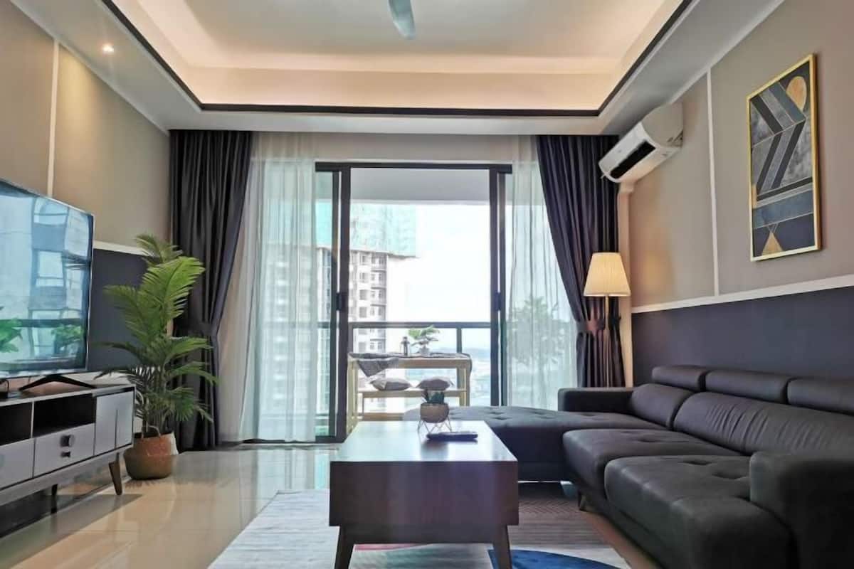 A modern living room with a sofa, a coffee table, a TV, and a large window with curtains.