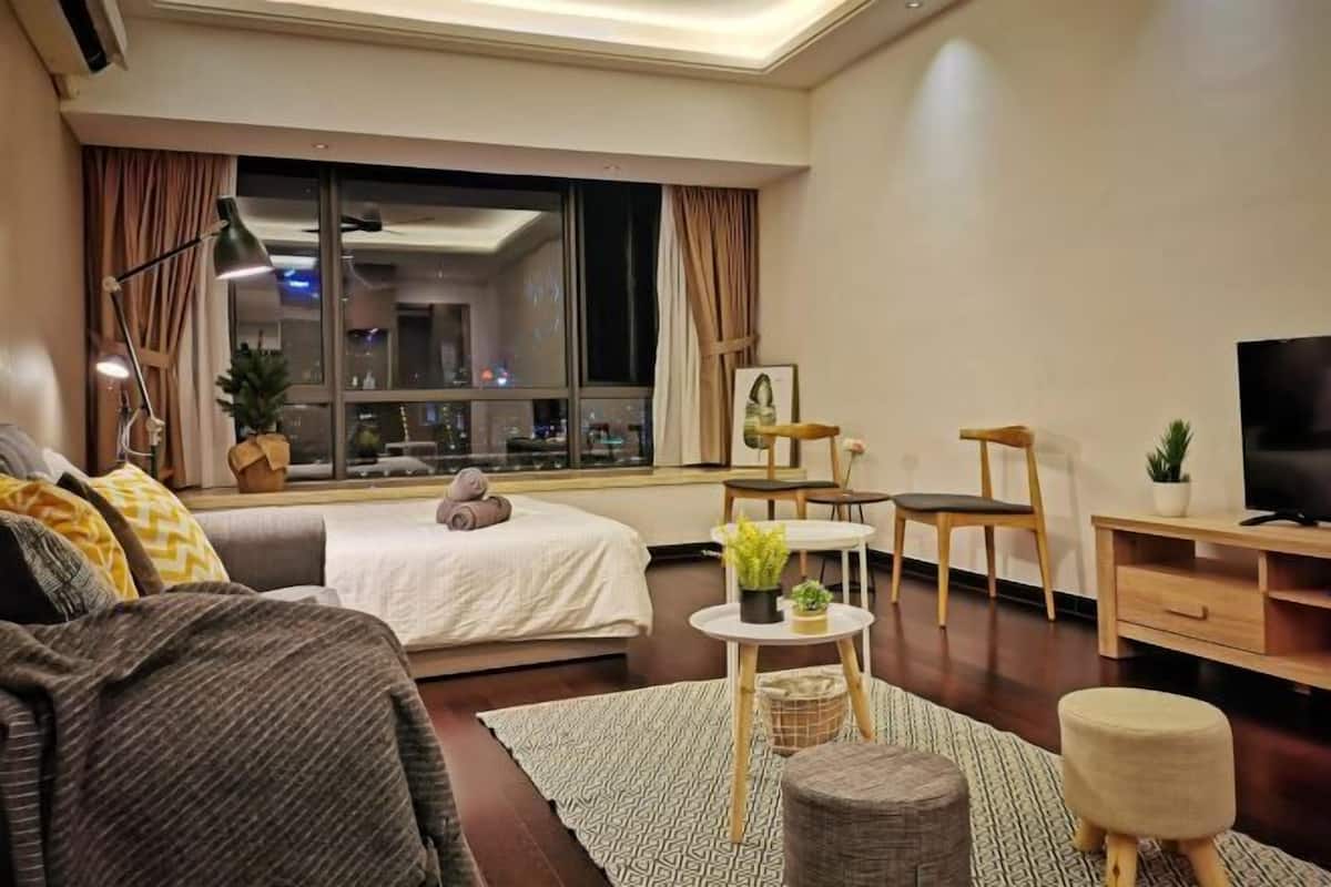 A modern hotel room with a bed, a sofa, a TV, a desk, and a window with a city view.