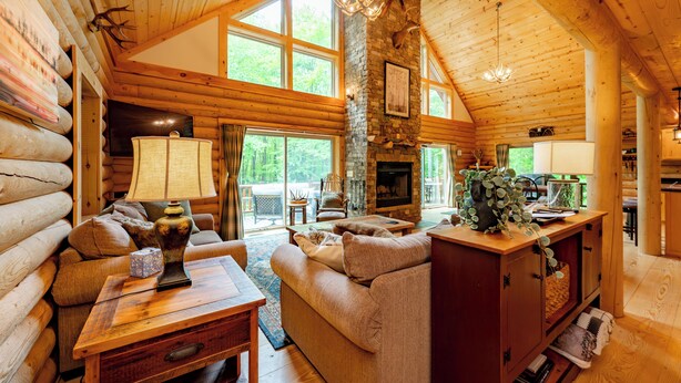 L’intérieur d’une cabane en rondins, avec une cheminée, des meubles en bois et de grandes fenêtres.