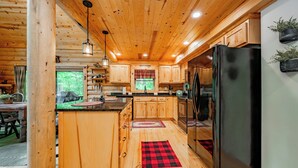 L’intérieur d’un chalet en bois comprend une cuisine avec des meubles en bois, un réfrigérateur noir et une fenêtre donnant sur un paysage verdoyant.