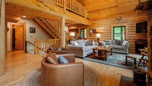 L’intérieur d’une cabane en rondins, avec un escalier en bois, deux canapés, une table basse et une cheminée.