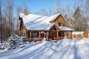 A wooden cabin with a porch, a chimney, and a snow-covered landscape.