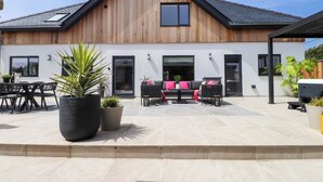 Une maison moderne avec une façade en bois, un patio doté de mobilier d’extérieur et de plantes en pot.