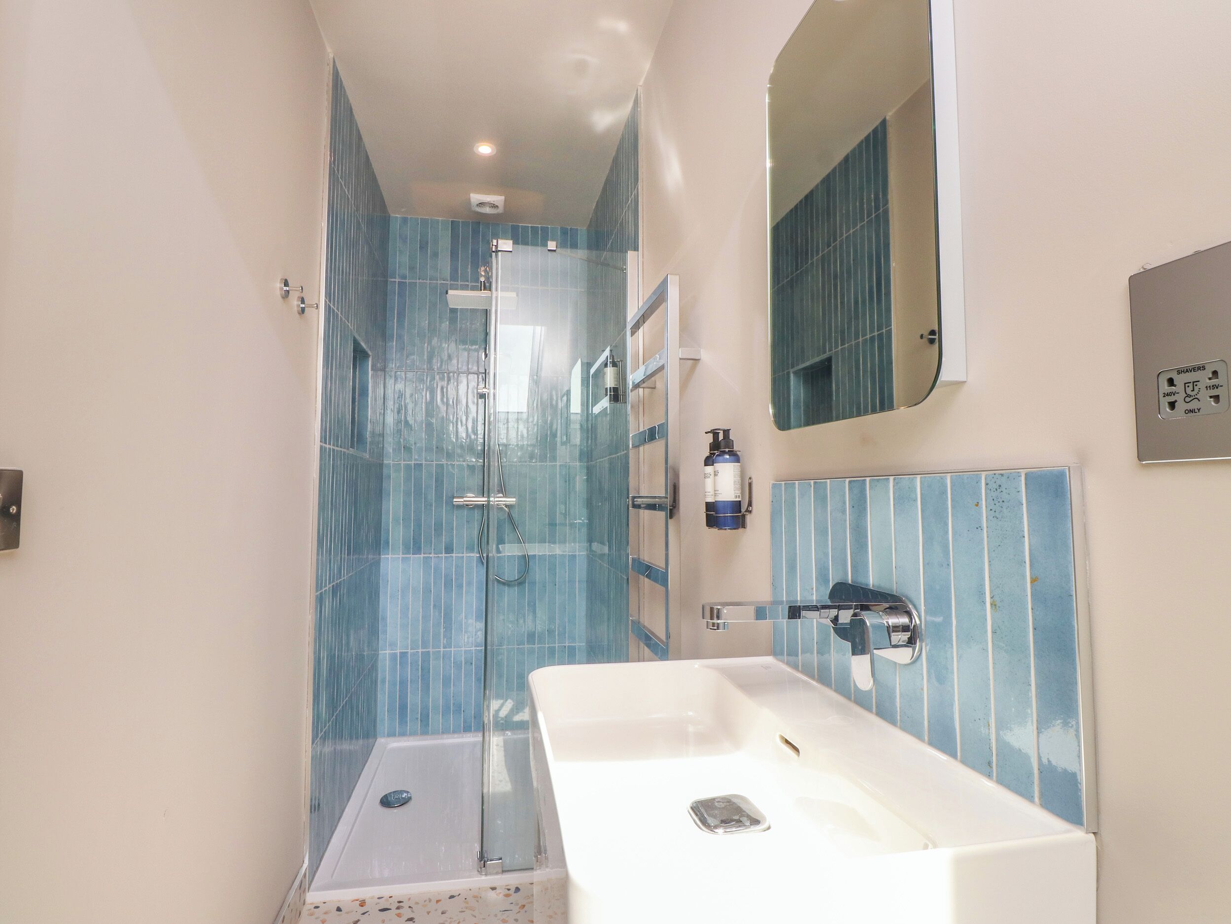 Une salle de bain moderne avec une douche à parois de verre, un lavabo blanc et un miroir au-dessus.