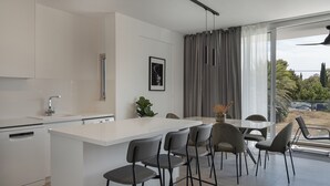 Eine moderne Küche mit einer zentralen Kochinsel, Barhocker und einem Essbereich mit Ausblick ins Freie.