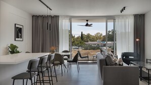 Ein modernes Wohnzimmer mit einer Couch, Sesseln, einem Essbereich mit Bar und einer großen Schiebeglastür, die zu einem Außenbereich führt.