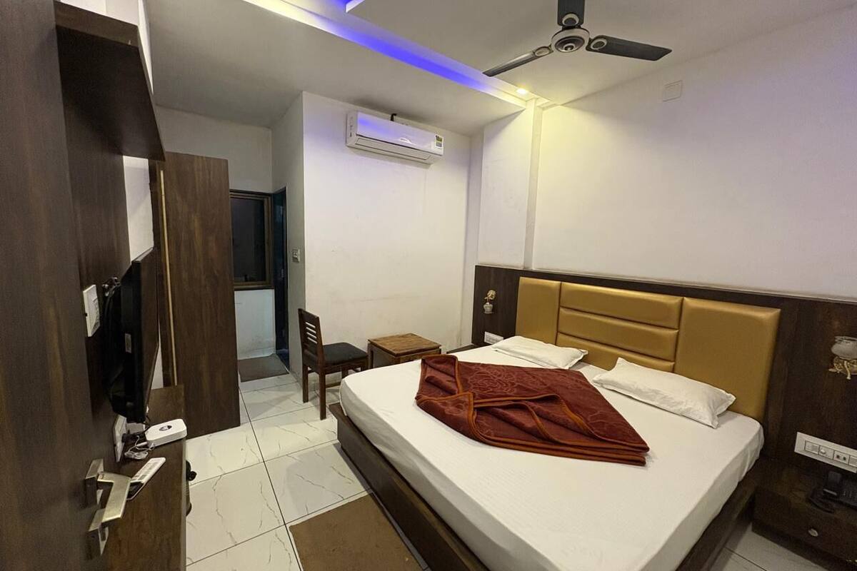 A hotel room with a bed, a desk, a chair, an air conditioning unit, and a ceiling fan.