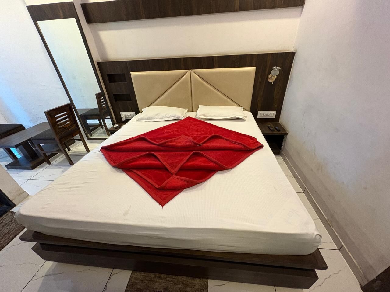 A neatly made bed with a red blanket, a wooden headboard, and a bedside table with a lamp.