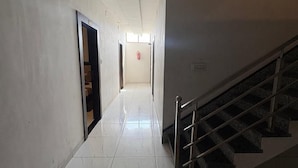 Un pasillo con una escalera a la derecha que conduce a un piso superior. El suelo está cubierto de baldosas y hay puertas a la izquierda.