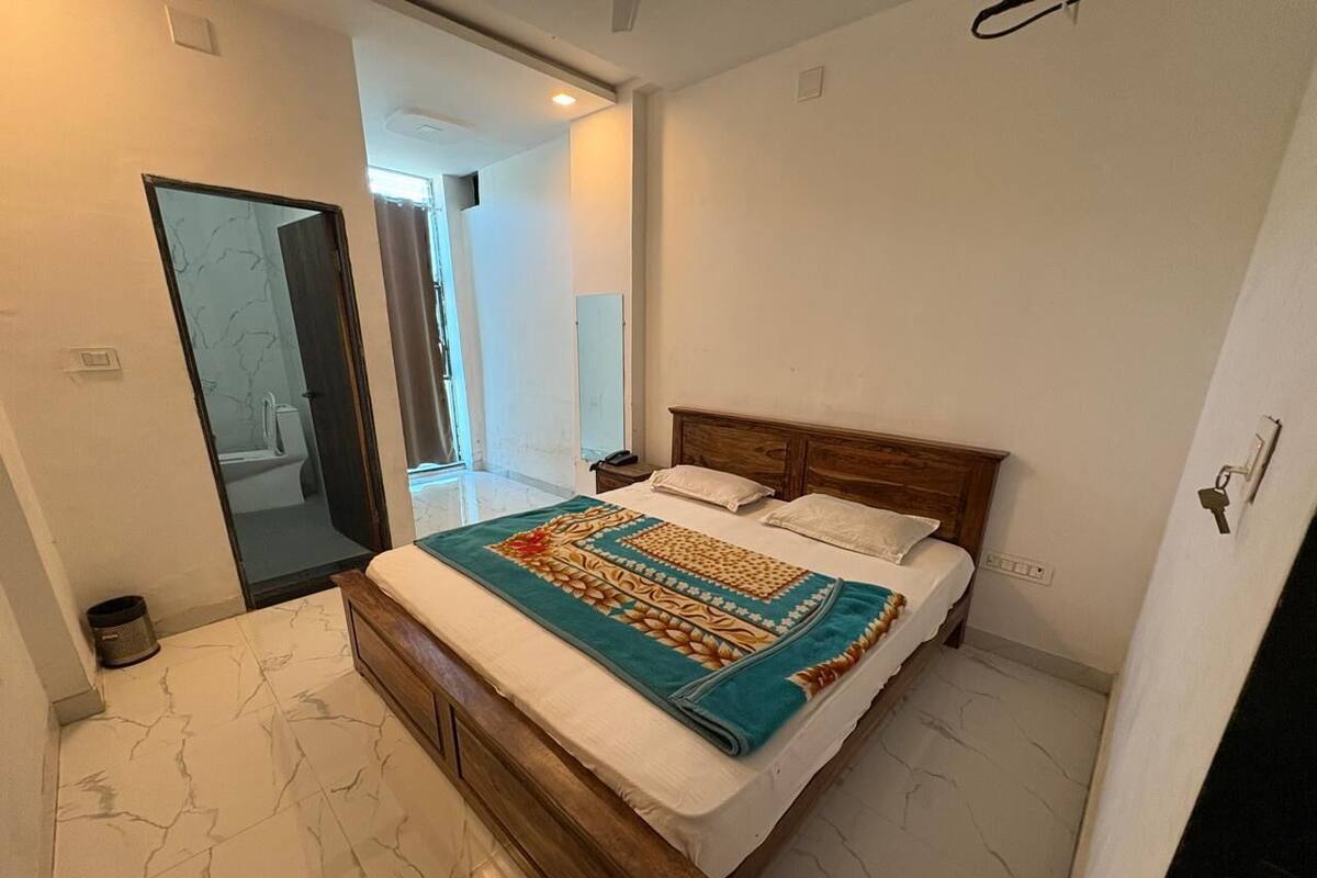 A bedroom with a bed, a wooden headboard, a bathroom visible through an open door, and a marble floor.