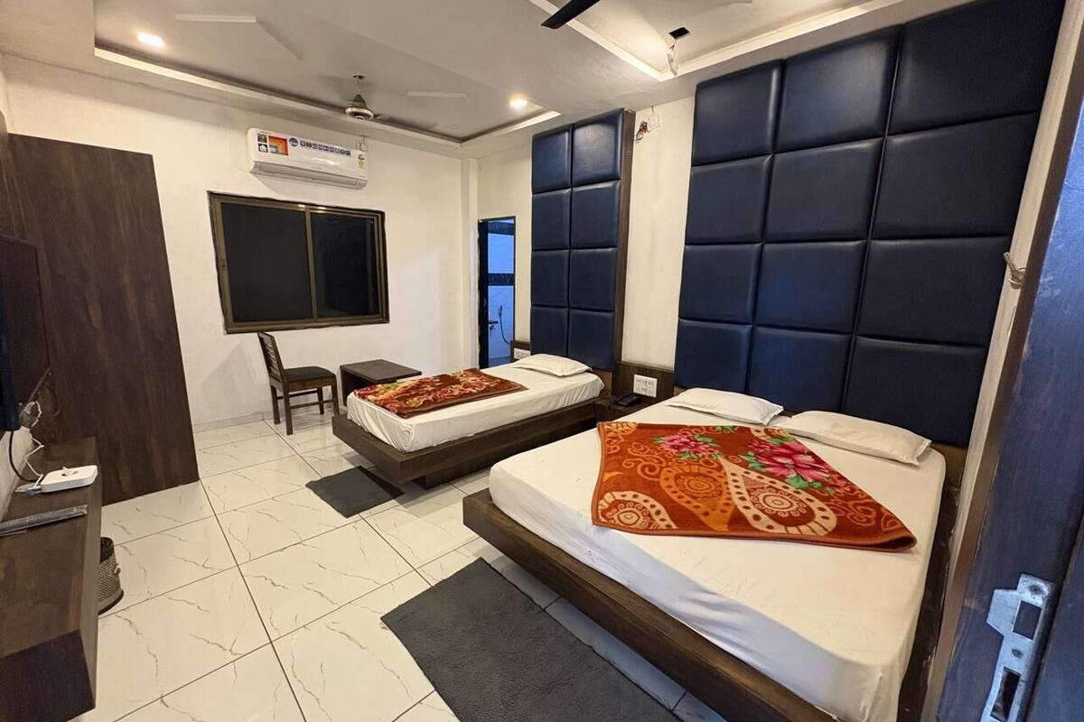 A hotel room with two beds, a desk, a chair, and a TV.
