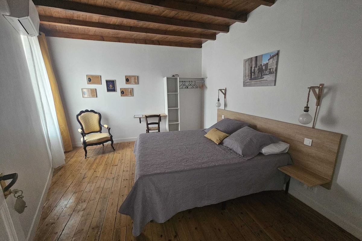 A bedroom with a wooden ceiling, a bed with grey bedding, a chair, a desk, and a wardrobe.