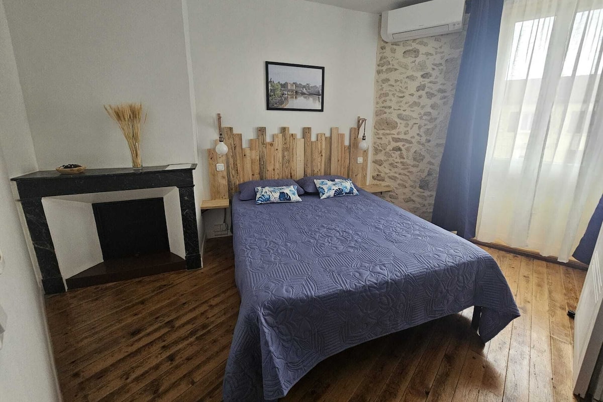 A bedroom with a bed, a small table, a picture on the wall, and a stone wall.