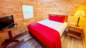 Una habitación con paneles de madera, una cama, un escritorio con una computadora y una lámpara.