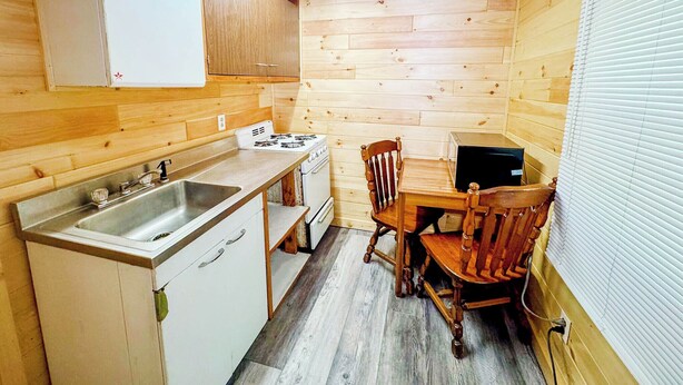 Una cocina pequeña con paredes de madera, un lavamanos, una estufa y una mesa de comedor con sillas.
