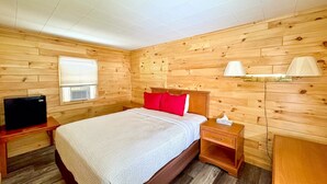 Un dormitorio con paneles de madera, una cama, mesitas de noche, un televisor y una lámpara.
