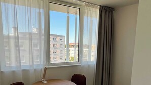 A room with a round table and two chairs, a window with curtains, and a view of buildings outside. - Comfort Studio in a Premium Residence- Sport/cinema (Huningue)