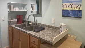 A kitchen with granite countertops, a stainless steel sink, wooden cabinets, and a built-in microwave. - Tiny House Retro Cabin (Umatilla)