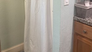 A bathroom with a shower curtain, a towel rack with a towel, a sink with a soap dish, and a wooden cabinet. - Tiny House Retro Cabin (Umatilla)