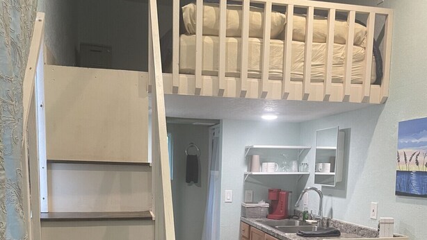 A compact living space with a loft bed, a kitchen area, and a small seating area. - Tiny House Retro Cabin (Umatilla)