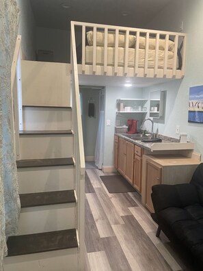 A compact living space with a loft bed, a kitchen area, and a small seating area.
