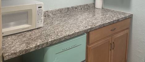 A kitchen with a microwave, teal cabinets, a granite countertop, and a painting on the wall.