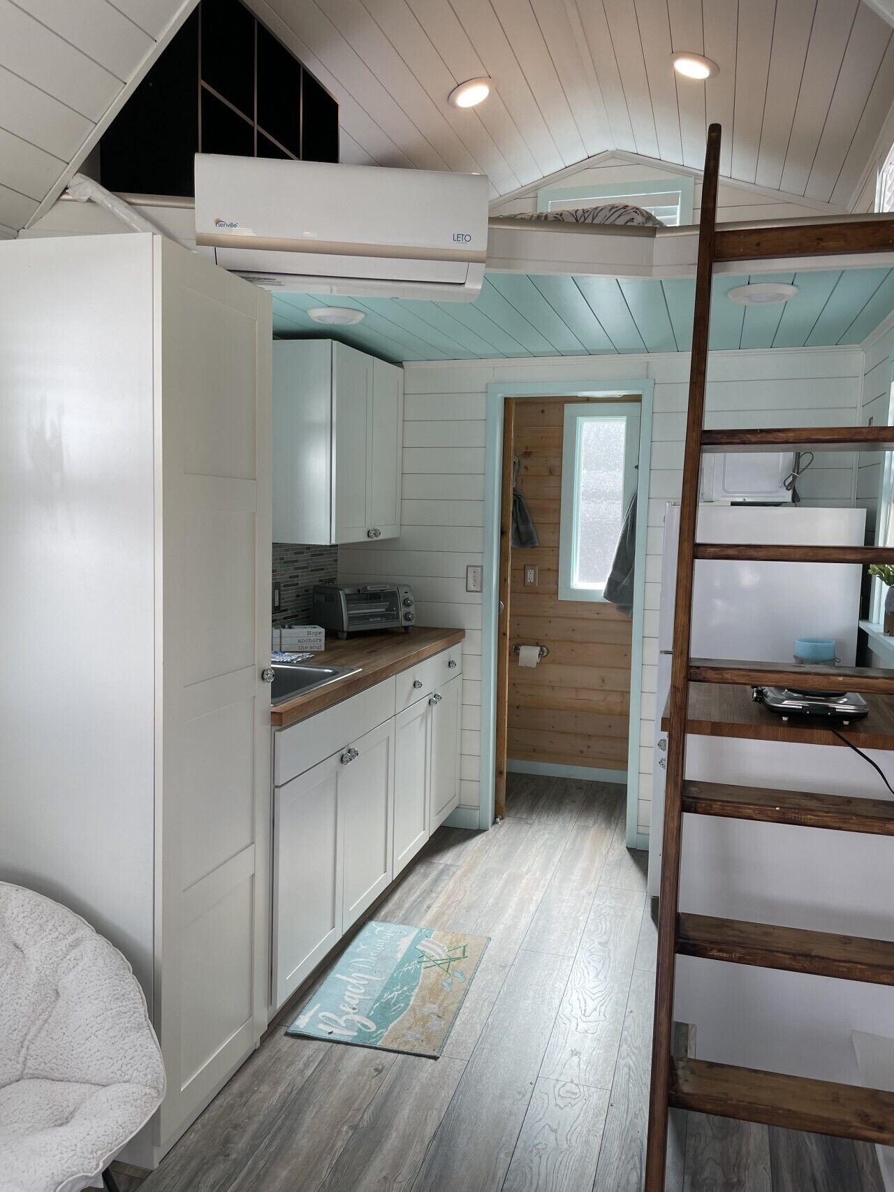 A compact kitchen with white cabinets, a wooden countertop, and a built-in microwave.