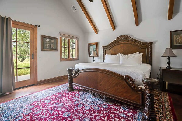 A bedroom with a large bed, wooden headboard, and a red patterned rug.