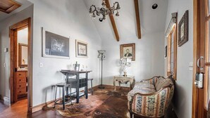 Ein Zimmer mit Holzbalkendecke, einem gemusterten Sofa, einem Schreibtisch mit Stuhl und gerahmten Bildern an den Wänden.