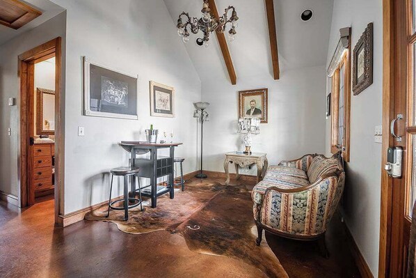 Quarto com teto de madeira, sofá estampado, escrivaninha com cadeira e quadros nas paredes.