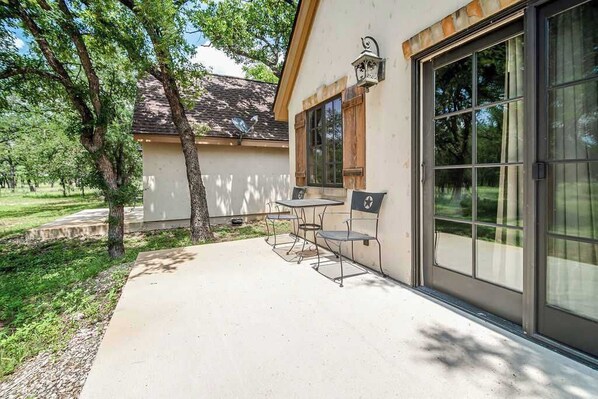 A patio with a table and chairs, a large sliding glass door, and a small outdoor light fixture.