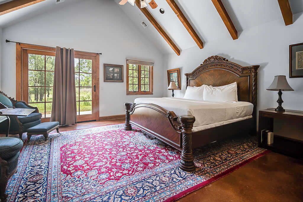 Une chambre avec un grand lit, un bureau et une chaise, offrant une vue sur les arbres à travers les fenêtres.