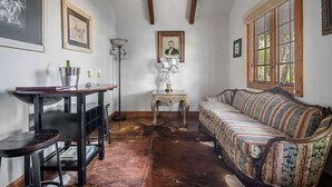 Ein Zimmer mit Holzboden, einem gemusterten Sofa, einem Tisch mit Lampe und gerahmten Bildern an den Wänden.